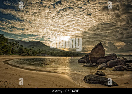 Ein Sonnenaufgang in Grand Anse Seychellen erzeugen eine ruhige Stimmung mit den frühen Morgen weichen Sonnenstrahlen durch die Makrele Himmel peeping Stockfoto