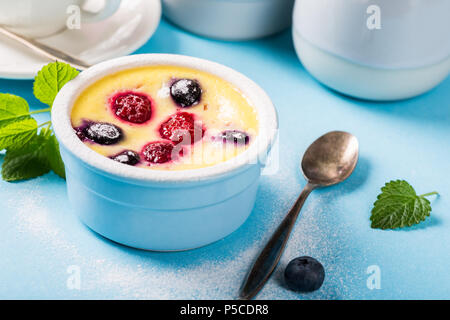 Berry clafouti. Traditionelle französische süße Frucht dessert Clafoutis mit Himbeeren und Blaubeeren auf blauem Hintergrund. Gesund glutenfreie Lebensmittel Konzept Stockfoto