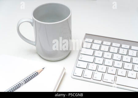 Eine Tasse Kaffee auf dem Schreibtisch, zwischen Tastatur und Zwischenablage Stockfoto