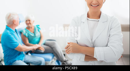 Frau Doktor mit Ihrer älteren Patienten im Hintergrund, im Vordergrund konzentrieren, auf lächelnde Teil der Doctor's Gesicht. Stockfoto