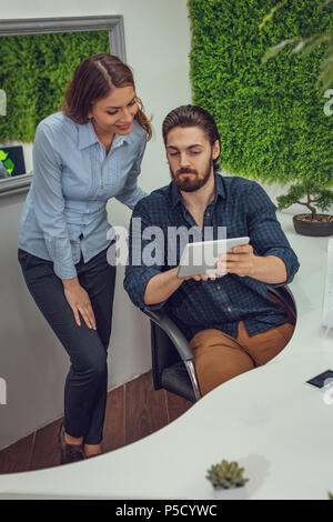 Clevere progressive junge Ingenieure arbeiten an digitalen Tablet auf einer ökologischen Bauvorhaben im Büro, reden über einige grüne Projekt. Stockfoto