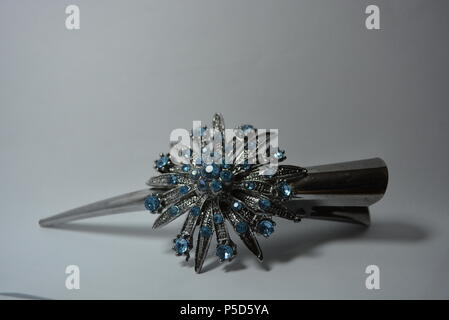 Schöner Damenschmuck, Stahl und eleganter Modeschmuck. Graue Metallhaarspange mit großer Metallblume aus blauen Steinen auf weißem Hintergrund Stockfoto