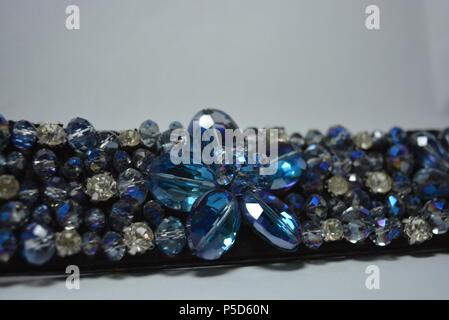 Damenschmuck, Stahl und eleganter Modeschmuck. Schwarzer Damengürtel mit elastischen Bändern, verziert mit abgeschrägten Einsätzen, blauen und weißen Steinen. Stockfoto