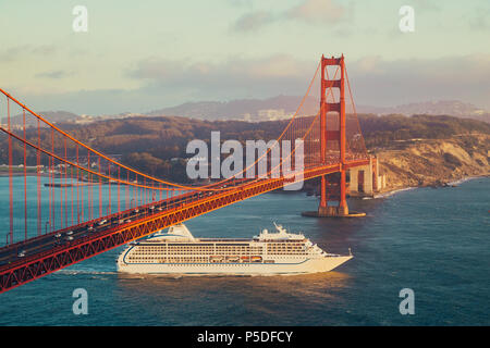Schönen Panoramablick auf Kreuzfahrtschiff, die berühmte Golden Gate Bridge mit Blick auf die Skyline von San Francisco im Hintergrund in wunderschönen goldenen Eveni