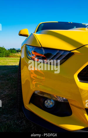Ein gelber Ford Mustang 5 Liter V8 GT Fastback Auto mit einem zweiten orange Ford Mustang, spiegelt sich in der scheinwerferlinse Stockfoto
