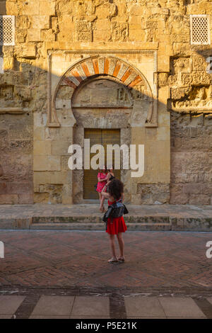 Junge Frauen, eine junge Frau fotografiert ihre Freunde, die vor einer maurischen Tür in der Außenwand der Mezquita, Cordoba, Spanien, posierten. Stockfoto