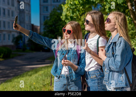 Drei Mädchen Freundin. Sommer in der Natur. In seinen Händen hält ein Smartphone. Macht Fotos auf dem Telefon. Das Konzept der Schule Freunde. In denim Kleidung Stockfoto