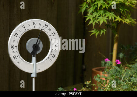 Circular thermometer shows a warm temperature during a sunny, sunlit summer's day in an english garden. Stockfoto