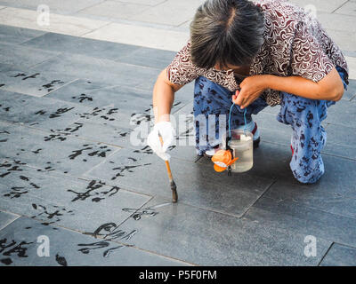 Peking, China - September 2017: Ältere Frau üben Wasser Kalligraphie, aber wegen der Hitze die chinesischen Zeichen verschwinden sofort und werden nicht gelesen Stockfoto