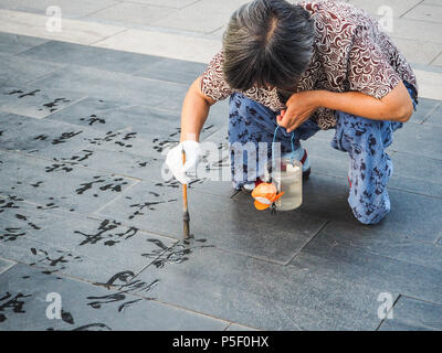 Peking, China - September 2017: Ältere Frau üben Wasser Kalligraphie, aber wegen der Hitze die chinesischen Zeichen verschwinden sofort und werden nicht gelesen Stockfoto