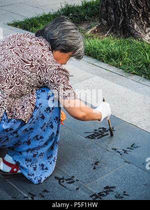 Peking, China - September 2017: Ältere Frau üben Wasser Kalligraphie, aber wegen der Hitze die chinesischen Zeichen verschwinden sofort und werden nicht gelesen Stockfoto