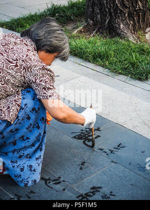 Peking, China - September 2017: Ältere Frau üben Wasser Kalligraphie, aber wegen der Hitze die chinesischen Zeichen verschwinden sofort und werden nicht gelesen Stockfoto