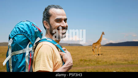 Lächelnder Mann mit Rucksack über afrikanische Savanne Stockfoto