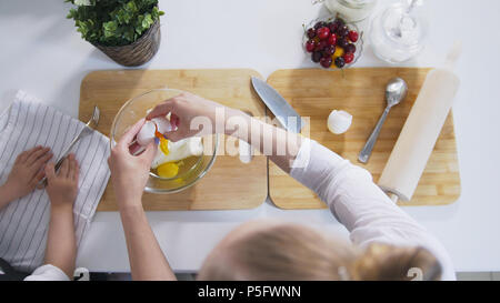 Mutter mit ihrer Tochter setzt rohe Eier in den Teig für Quark Pfannkuchen Stockfoto