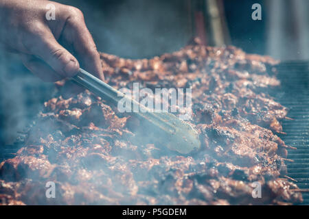 Fleisch am Spieß gebraten auf dem Grill im Freien, sichtbare Hand der Koch. Stockfoto