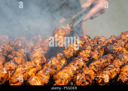 Fleisch am Spieß gebraten auf dem Grill im Freien, sichtbare Hand der Koch. Stockfoto