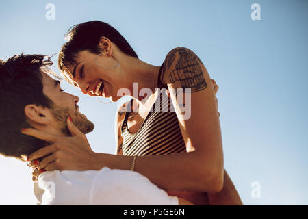 Schönes Paar Flirten im Freien. Frau in die Arme ihres Freundes beim Stehen im Freien an einem sonnigen Tag. Stockfoto