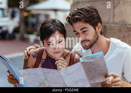 Touristische Paar mit Hilfe einer Karte, um die Route zu Ihrem Ziel zu finden. Mann und Frau Reisende in der Nähe der Bürgersteig sitzen und Kontrolle einer Karte. Stockfoto