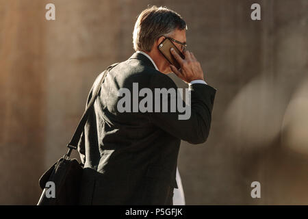 Mann in formelle Kleidung sprechen über Mobiltelefon während Fahrten zum Büro. Büro gehen, Person zu Fuß auf der Straße Gespräch am Handy. Stockfoto