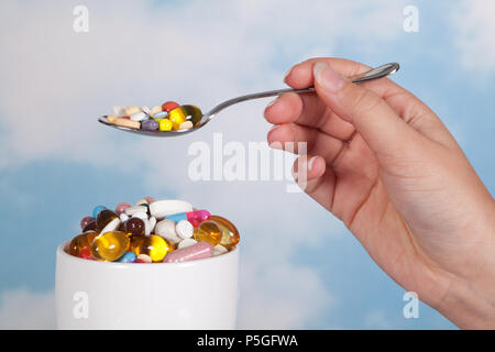 Hand mit einem Esslöffel Pillen über einer Schüssel mit Tabletten gefüllt Stockfoto