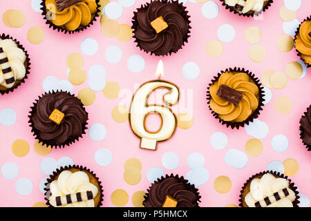 Nummer 6 Gold Kerze mit Cupcakes gegen ein Pastell rosa Hintergrund Stockfoto