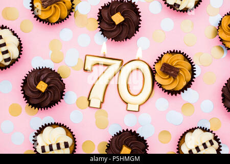 Nummer 70 goldene Kerze mit Cupcakes gegen ein Pastell rosa Hintergrund Stockfoto