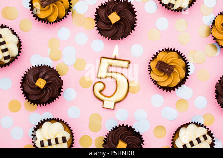 Nummer 5 Gold Kerze mit Cupcakes gegen ein Pastell rosa Hintergrund Stockfoto