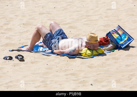 Bournemouth, Dorset, Großbritannien. Juni 2018. Wetter in Großbritannien: Sonnenanbeter begeben sich an einem weiteren schönen, sonnigen Tag mit ungebrochenem blauem Himmel und Sonnenschein zu den Stränden von Bournemouth. Eine schöne kühlende Brise macht die Hitze heute erträglicher. Mann sonnt sich am Strand mit Hut, der sein Gesicht bedeckt. Stockfoto