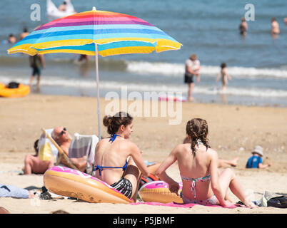 Lyme Regis, Dorset, Großbritannien. 27.Juni 2018. UK Wetter. Warm und sonnig in Lyme Regis, als die Hitzewelle weiter. Zwei junge Frauen sonnen unter einem hellen Sonnenschirm am Strand von der Küstenstadt Lyme Regis. Credit: DWR/Alamy Leben Nachrichten. Stockfoto