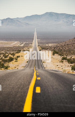 Classic panorama Blick auf eine endlose gerade Straße durch die karge Landschaft des amerikanischen Südwestens mit extremer Hitze Dunst auf einen schönen s Stockfoto