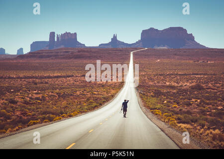 Classic panorama Blick auf junge Person zu Fuß auf den berühmten Forrest Gump highway im Monument Valley am Mittag, Arizona, USA Stockfoto