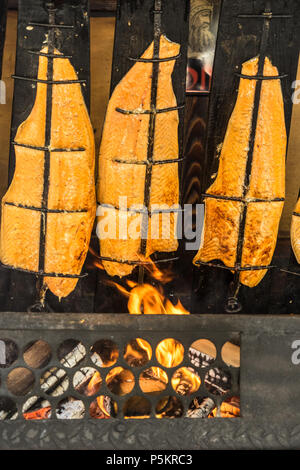 Vorbereitung der Flamme Lachs über dem offenen Feuer der einen offenen Kamin mit Holz beladen, Deutschland Stockfoto