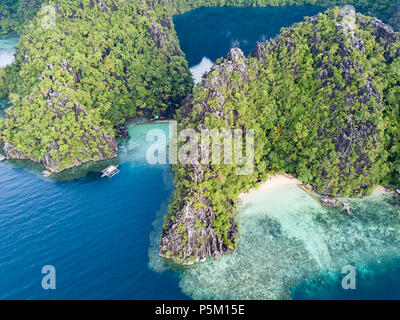 Aus der Vogelperspektive sehen Sie dramatische Kalkstein-Karstklippen und versteckte türkisfarbene Lagune mit Boot, El Nido, Palawan, Philippinen Stockfoto