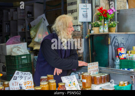 9. Mai 2018 eine schmuddelig aussehende Besitzer Stall mit einem langen blonden Bart auf seine Ellenbogen zwischen Kunden am Mahane Yehuda Markt Jerusalem lehnt. Stockfoto