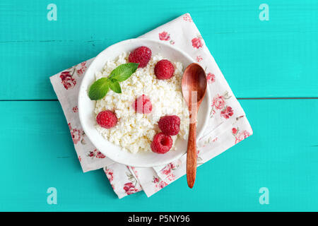 Ricotta mit Himbeeren in eine Schüssel auf Türkis Holz- Hintergrund. Quark, Hüttenkäse, tvorog. Gesunde Ernährung, gesunde Lebensweise, Sommer dess Stockfoto