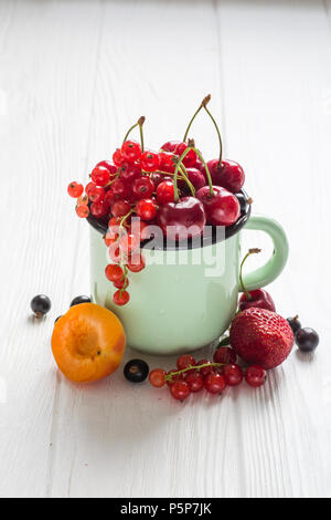 Verschiedene Arten von Beeren in Emaille Tasse Tee auf einem weißen Tisch Stockfoto