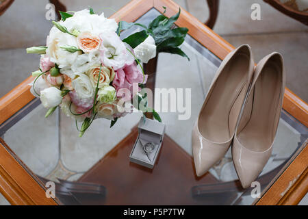Trauringe mit Diamanten, Schuhe und eine Hochzeit Strauß auf einem Glastisch Stockfoto