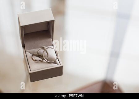 Trauringe mit Diamanten in einer Geschenkbox auf einem Glastisch Stockfoto