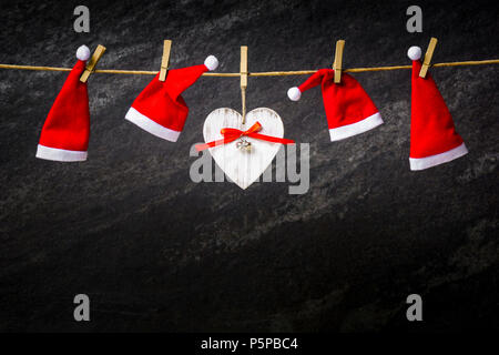 Dunkle Weihnachten Hintergrund mit Nikolausmützen und Herz auf einem Seil Stockfoto