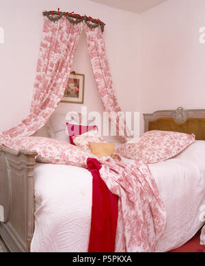 Land Schlafzimmer mit Mauerkrone mit pink + weiß Toile-de-Jouy Vorhänge über vintage Französisches Bett mit passenden Toile Kissen und Werfen Stockfoto