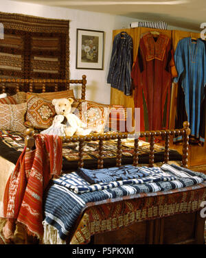 An der Wand über dem Bett mit gedrehtem Holz- Spindeln mit Kissen im Schlafzimmer voller ethnischer Kleider und Teppiche gestapelt Stockfoto