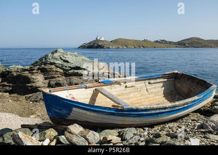 Kleine Holz- Boot vertäut Am felsigen Ufer auf der Insel Kea (Tzia) mit Leuchtturm in der Ferne, Kykladen Inseln der Ägäis, Griechenland. Stockfoto