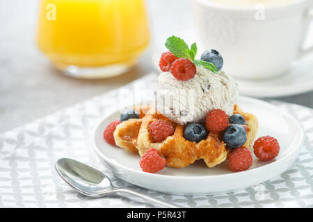 Selbstgemachte Waffeln mit Eis und frischen Beeren - Himbeeren, Heidelbeeren. Leckere Nachspeise, Cappuccino und Orangensaft auf dem Tisch. Selektive foc Stockfoto