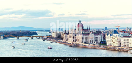 Kreuzfahrtschiffe bei Sonnenuntergang auf der Donau. Warm Sky auf dem Wasser widerspiegeln. Berühmte Parlament und Stadt für den Hintergrund. Budapest, Ungarn Stockfoto