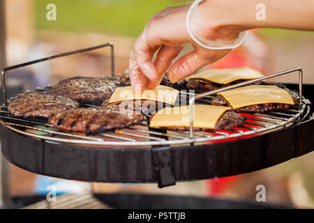 Die Hand des Menschen, der Verbreitung der Käse auf den Burgern Stockfoto