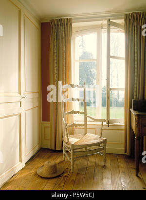 Rush sitzen ladderback Stuhl vor der geöffneten Fenster im französischen Landhausstil Schlafzimmer mit Holzböden Stockfoto