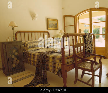 Bemalte Schrank neben dem hölzernen Bett mit Bettwäsche in Portugiesisch Schlafzimmer mit französischen Fenstern Stockfoto