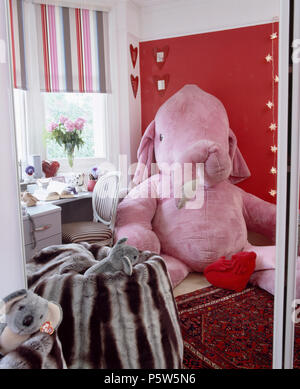 Großen Pink Velours Elefant gegen rote Wand im Kinderzimmer mit Velour Bean Bag und Fenster mit Rosa + Grau gestreiften blind Stockfoto