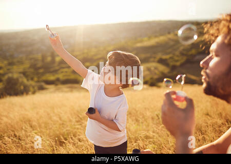 Vater und Sohn spielen mit Seifenblasen in der Natur Stockfoto