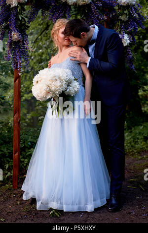 Die Braut und der Bräutigam stand auf der Arch, mit Blumen geschmückt, mit einem großen Blumenstrauß aus den weißen Pfingstrosen. Registrierung vor Ort im Park Hochzeit gehen ein Stockfoto